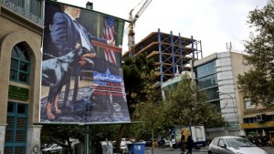A poster depicting an American negotiator wearing a suit jacket and tie at a negotiating table and a dog to his side is displayed in Palestine Square in Tehran, Iran, on Sunday, October 27, 2013. (AP Photo/Ebrahim Noroozi)
