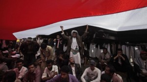 In this Saturday, March 5, 2011, file photo, anti-government protesters take shelter from the sun under their national flag during a demonstration demanding the resignation of Yemeni President Ali Abdullah Saleh in Sana'a, Yemen. (AP Photo/Muhammed Muheisen, File)