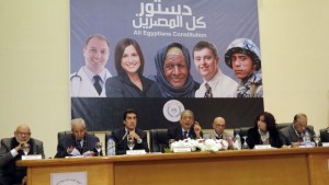 Egypt's constitutional committee chairman Amr Mussa (C) gestures as he sits alongside other officials under a poster to promote a new draft constitution wish a slogan reading in Arabic, "All Egyptians Constitution" , in Cairo on December 15, 2013. An Egyptian official has resigned amid controversy over the poster to promote a new draft constitution that featured images of non-Egyptians and misspelled "Egyptians" in Arabic, state media. Amgad Abdel Ghaffar, head of the State Information Service, the government's media arm, had already apologised for the poster, which featured Caucasian-looking images under the caption: "All Egyptians Constitution." AFP PHOTO/HOSAN FADL