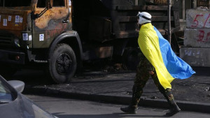 A protester covered with a Ukrainian national flag passes by a destroyed truck near the Ukrainian Parliament building in downtown of Kiev, Ukraine, on February 24, 2014. (EPA/MAXIM SHIPENKOV)