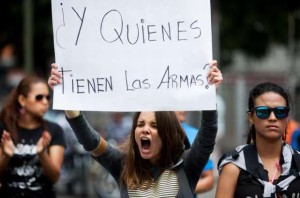 A student from the Alejandro Humboldt University holds up a sign that reads in Spanish "And who has the weapons?" as she shouts slogans against Venezuela's President Nicolas Maduro to protest yesterday's killing of Bassil Da Costa, at the Alejandro Humboldt University where he studied in Caracas, Venezuela, Thursday, Feb. 13, 2014.