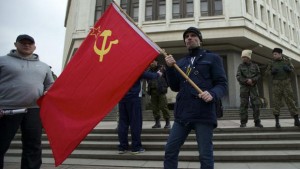 A local resident holds a Soviet flag as members of Cossack militia guard the local parliament building in Simferopol, in Ukraine’s Crimea region, on Thursday, March 6, 2014. (AP Photo/Ivan Sekretarev)