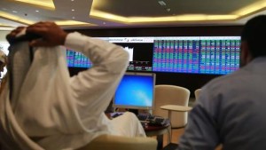 Traders speak with each other as they sit behind their desks in front of the Qatar stock exchange board, in Doha on February 4, 2014. (Reuters/Mohammed Dabbous)