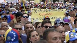 An opposition activists shows a sign reading "Cuban mercenaries out of the National Guard" during a protest in front of the OAS headquarters building in Caracas on March 3, 2014. The latest wave of protests, which erupted on February 4 and up to now has left at least 18 people killed and 250 injured, has grown into the biggest threat to President Nicolas Maduro since he succeeded socialist icon Hugo Chavez last year. AFP PHOTO/JUAN BARRETO
