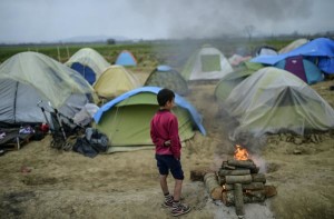 A boy stands next to a fire at a makeshift camp set by refugees and migrants stranded by the Balkan border blockade, on April 3, 2016 near the village of Idomeni at the Greek Macedonian border