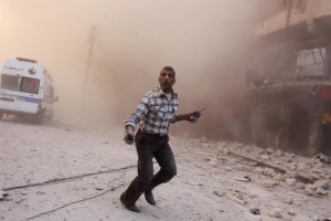 A man holding walkie-talkies runs towards a site damaged by what activists said were barrel bombs dropped by warplanes loyal to Syria's President Assad, in Aleppo
