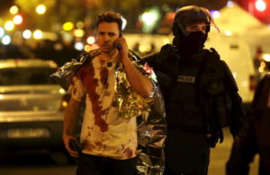 ATTENTION EDITORS - VISUAL COVERAGE OF SCENES OF INJURY A French policeman assists a blood-covered victim near the Bataclan concert hall following attacks in Paris, France, November 14, 2015. Gunmen and bombers attacked busy restaurants, bars and a concert hall at locations around Paris on Friday evening, killing dozens of people in what a shaken French President described as an unprecedented terrorist attack REUTERS/Philippe Wojazer