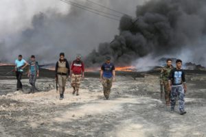 Tribal fighters walk as fire and smoke rises from oil wells, set ablaze by ISIS militants before ISIS militants fled the oil-producing region of Qayyara