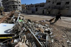 A woman walks past debris along a street in Aleppo's Belleramoun Industrial Zone