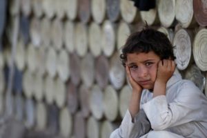 Boy looks on as he sits next to a hut at a camp for people displaced by the war near Sanaa, Yemen