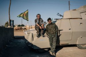 Lucas Chapman, left, and Brace Belden, U.S. volunteers with the People’s Protection Units, or YPG, pose for a portrait next to a homemade armored vehicle in a rear base near Tal Samin, Syria.