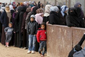 Syrian refugees stand in line as they wait for aid packages at Al Zaatari refugee camp