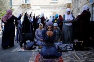 Palestinian women pray as others shout slogans outside the compound known to Muslims as Noble Sanctuary and to Jews as Temple Mount, in Jerusalem's Old City