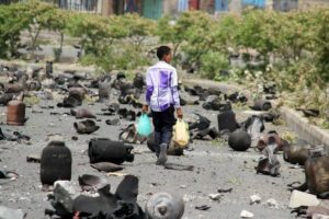 A boy walks on a street littered with cooking gas cylinders after a fire and explosions destroyed a nearby gas storage during clashes between fighters of the Popular Resistance Committees and Houthi fighters earlier today, in Taiz