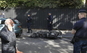 Police officers stand next to a burnt scooter outside the office of Jordan's military attache in Paris